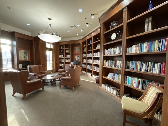 living area with wall of books, carpet, visible vents, and built in features