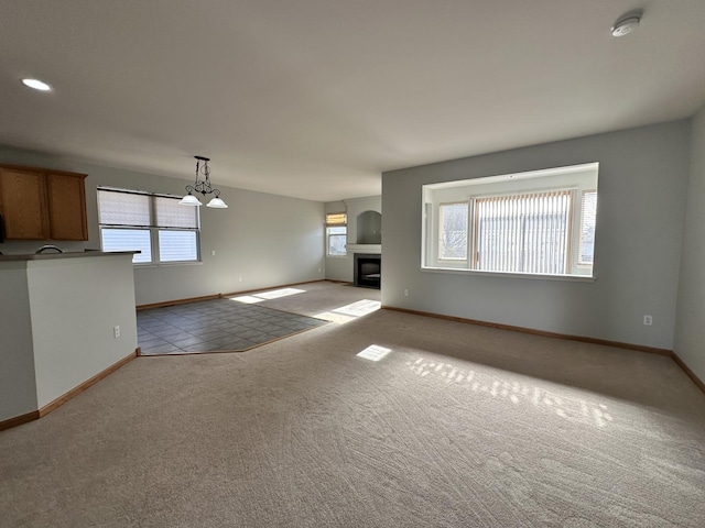 unfurnished living room featuring baseboards, a glass covered fireplace, and light colored carpet