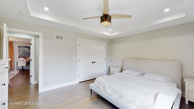 bedroom featuring dark wood-type flooring, a raised ceiling, visible vents, and baseboards