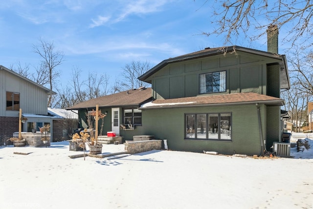 snow covered house featuring a chimney, cooling unit, and brick siding