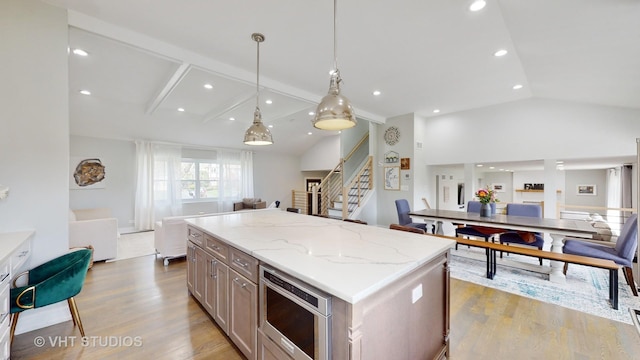 kitchen featuring open floor plan, a center island, vaulted ceiling, light wood-type flooring, and pendant lighting