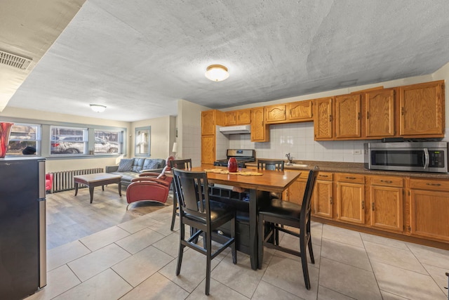 kitchen with brown cabinets, radiator, visible vents, appliances with stainless steel finishes, and under cabinet range hood