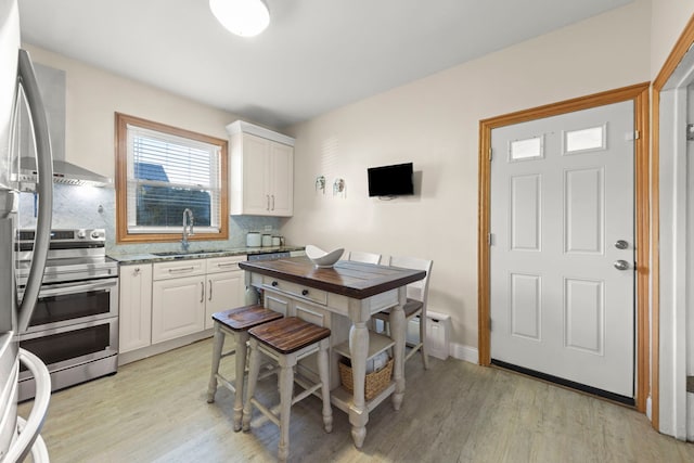 kitchen featuring range with two ovens, light wood-type flooring, white cabinets, and a sink