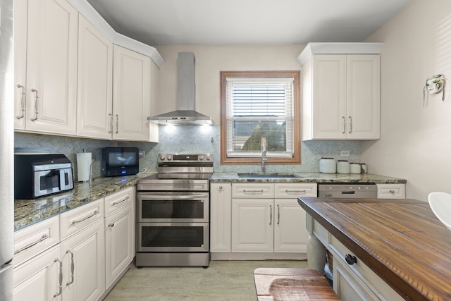 kitchen featuring wood counters, a sink, white cabinetry, wall chimney range hood, and appliances with stainless steel finishes