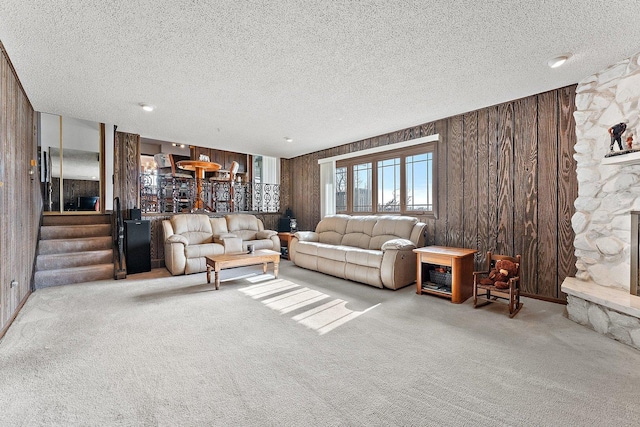 carpeted living room with a stone fireplace, a textured ceiling, and wood walls