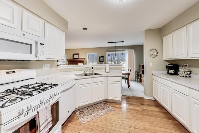 kitchen with light wood-style flooring, a peninsula, white appliances, white cabinetry, and a sink