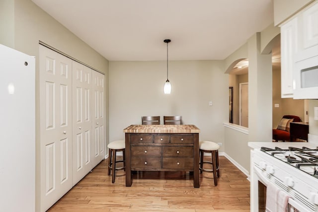 dining area with light wood finished floors, arched walkways, and baseboards