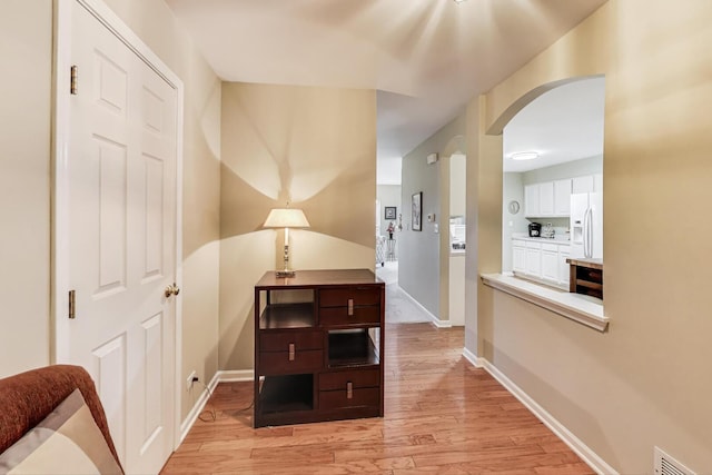 corridor featuring visible vents, arched walkways, light wood-style floors, and baseboards