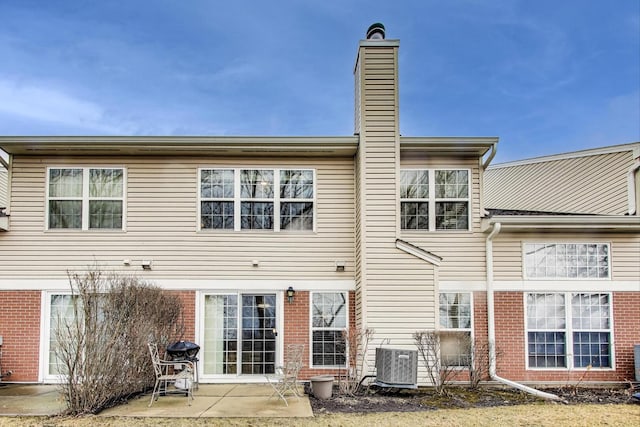 back of property with central AC unit, a chimney, and a patio area