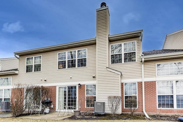 rear view of house with a patio, brick siding, central AC, and a chimney