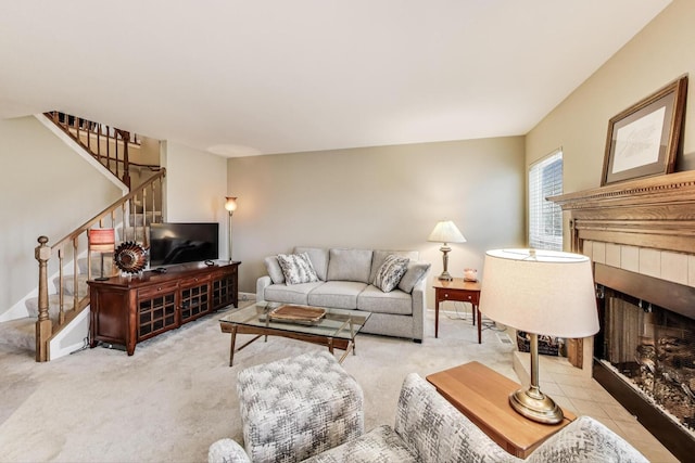 living area featuring stairs, a tiled fireplace, and carpet floors