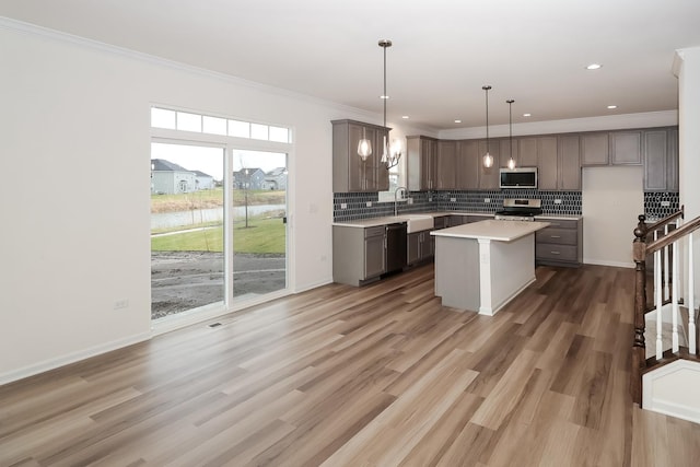 kitchen featuring crown molding, hanging light fixtures, backsplash, stainless steel appliances, and a kitchen island