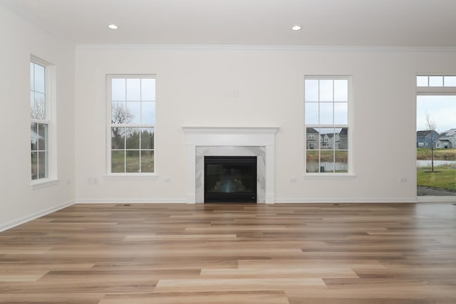 unfurnished living room with ornamental molding, a high end fireplace, and light hardwood / wood-style floors