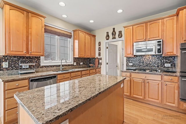 kitchen with light wood finished floors, appliances with stainless steel finishes, a sink, and light stone countertops