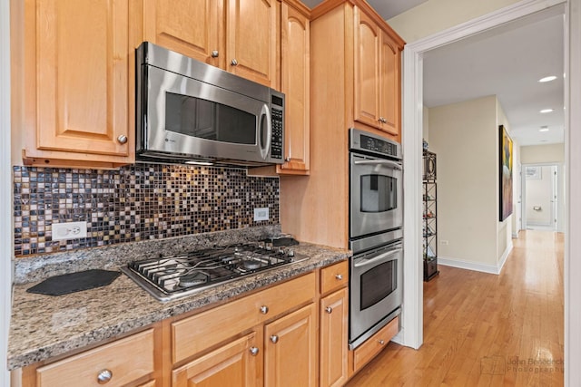 kitchen featuring light wood finished floors, stainless steel appliances, decorative backsplash, light stone countertops, and baseboards