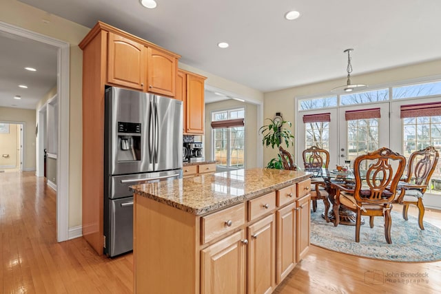 kitchen with light stone countertops, stainless steel fridge, light wood finished floors, and a center island