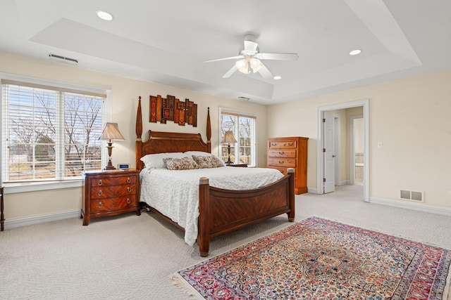 bedroom with light colored carpet, a tray ceiling, visible vents, and baseboards