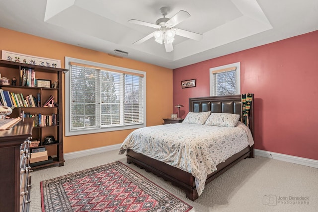 carpeted bedroom with ceiling fan, a raised ceiling, visible vents, and baseboards