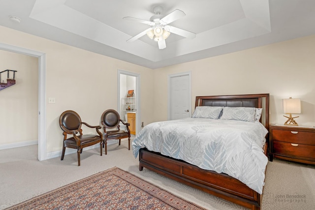 carpeted bedroom featuring ensuite bath, a raised ceiling, a ceiling fan, and baseboards