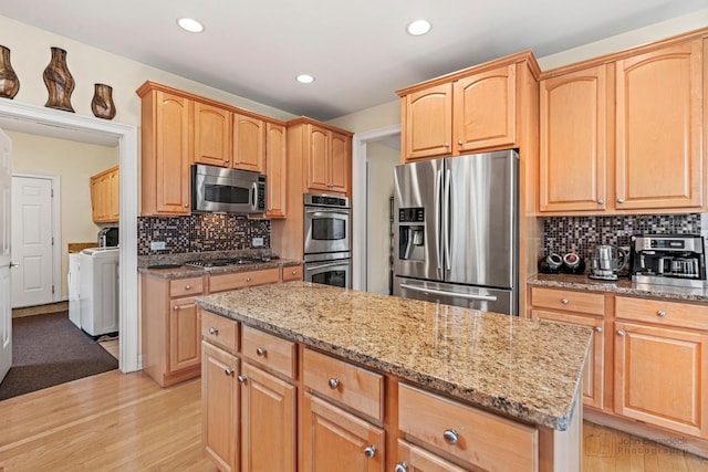 kitchen featuring appliances with stainless steel finishes, light wood-type flooring, independent washer and dryer, and light stone counters