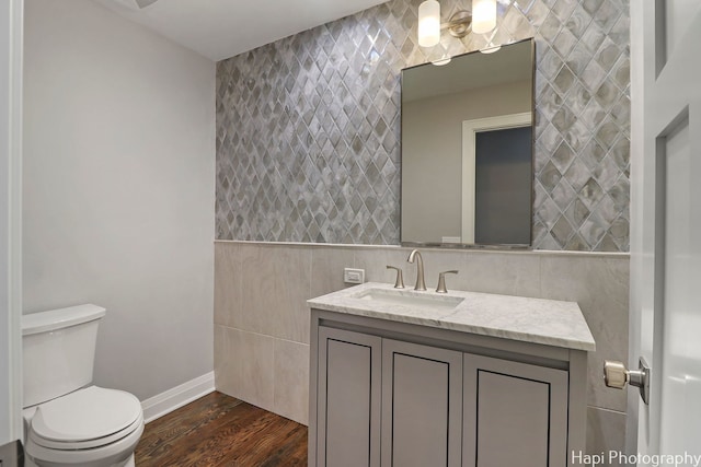 bathroom with toilet, wood-type flooring, tile walls, vanity, and decorative backsplash