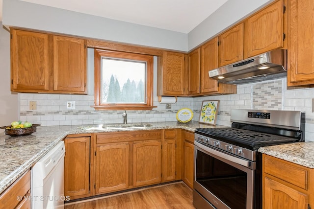 kitchen featuring light wood finished floors, stainless steel gas stove, white dishwasher, a sink, and under cabinet range hood