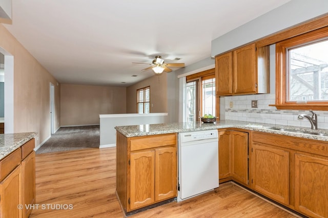 kitchen with a sink, light wood-style floors, a peninsula, and dishwasher