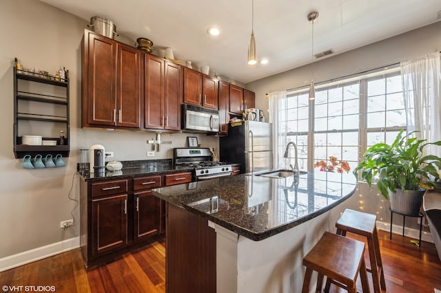 kitchen featuring baseboards, dark wood finished floors, a sink, stainless steel appliances, and a kitchen breakfast bar