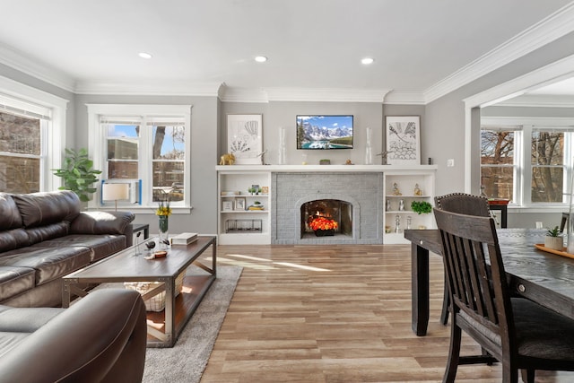 living room featuring ornamental molding, a brick fireplace, a wealth of natural light, and light wood-style floors