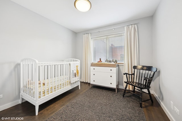 bedroom featuring a crib, dark wood-style floors, and baseboards