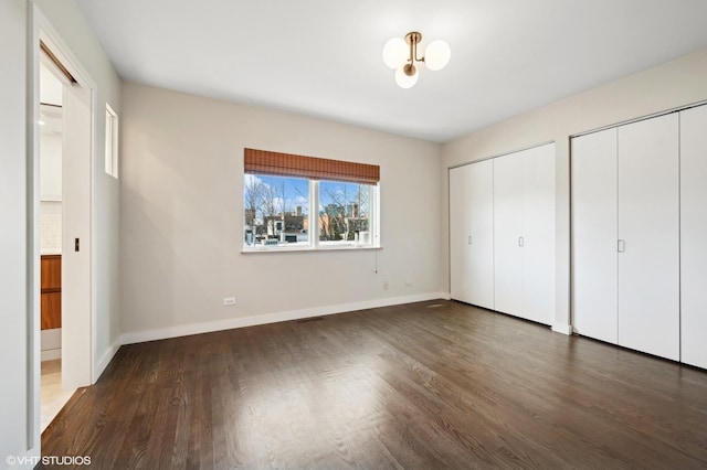 unfurnished bedroom featuring baseboards, visible vents, multiple closets, and wood finished floors