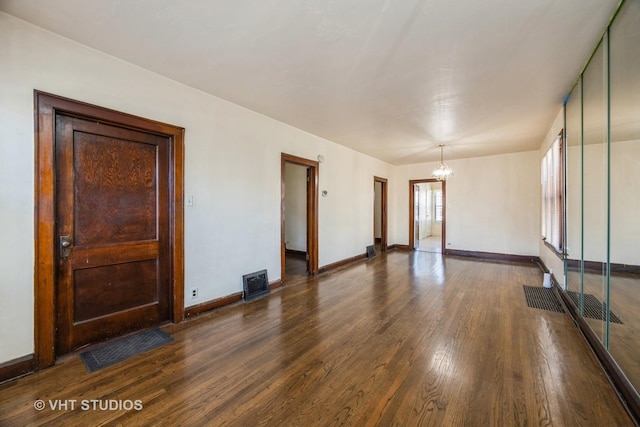 unfurnished room featuring an inviting chandelier, visible vents, baseboards, and dark wood-type flooring