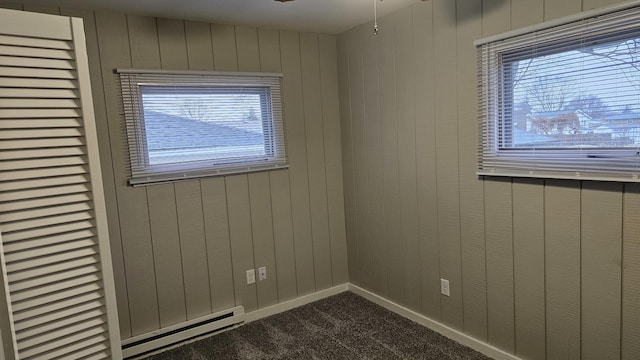 unfurnished room featuring carpet flooring, baseboard heating, and wood walls