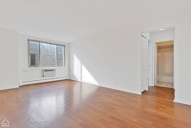 spare room featuring baseboard heating, light wood-type flooring, a wall unit AC, and baseboards