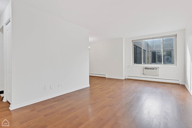 spare room with a baseboard radiator, a wall mounted air conditioner, baseboards, and wood finished floors