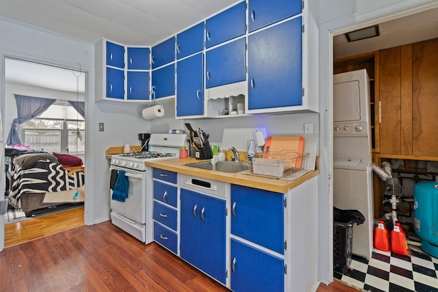 kitchen featuring sink, blue cabinetry, white gas range oven, and stacked washer / dryer