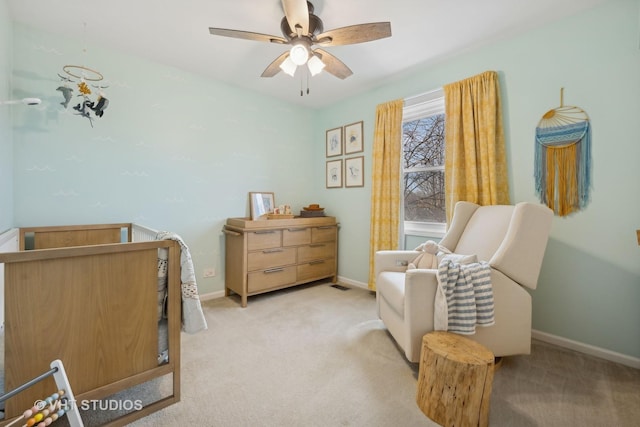 bedroom featuring a nursery area, light colored carpet, and ceiling fan