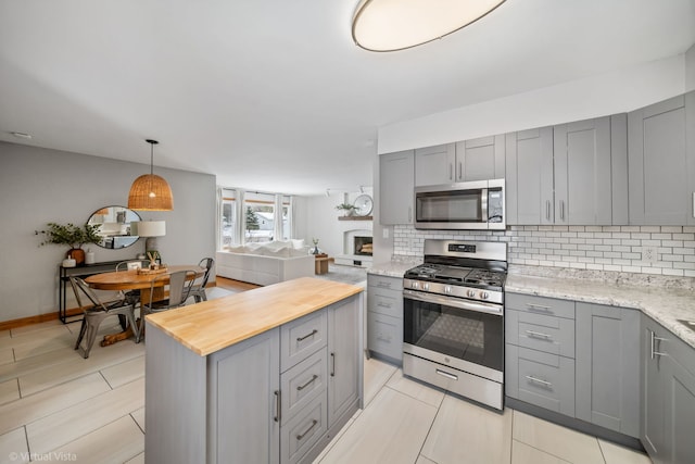 kitchen with backsplash, appliances with stainless steel finishes, light stone counters, and gray cabinetry