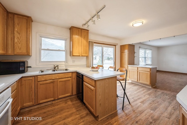 kitchen with black appliances, a sink, a kitchen breakfast bar, wood finished floors, and a peninsula