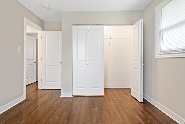 unfurnished bedroom with a closet, baseboards, and dark wood-style flooring