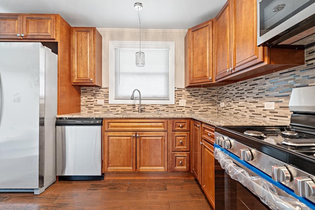 kitchen with appliances with stainless steel finishes, brown cabinets, hanging light fixtures, light stone countertops, and a sink