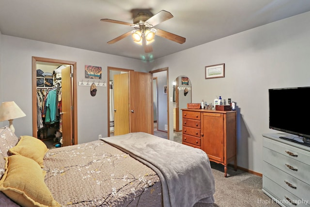 bedroom featuring light carpet, baseboards, ceiling fan, a walk in closet, and a closet