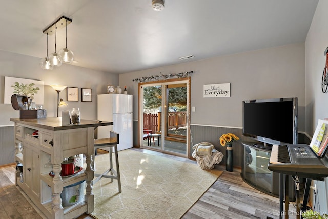 kitchen featuring visible vents, wainscoting, freestanding refrigerator, light wood finished floors, and pendant lighting