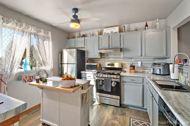 kitchen with under cabinet range hood, stainless steel appliances, a sink, light countertops, and dark wood finished floors