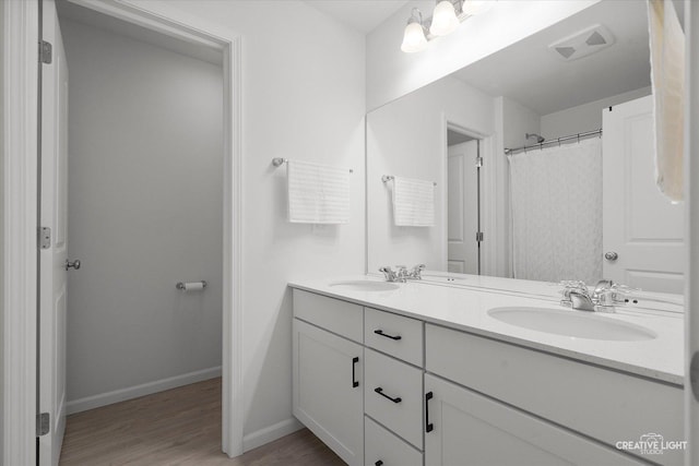 bathroom with double vanity, baseboards, visible vents, wood finished floors, and a sink