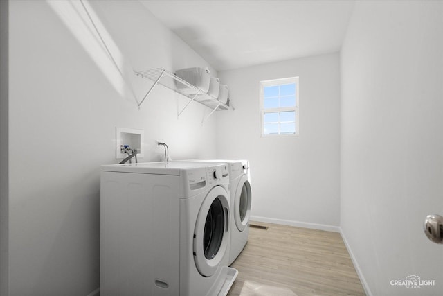 clothes washing area featuring laundry area, light wood finished floors, washing machine and dryer, and baseboards