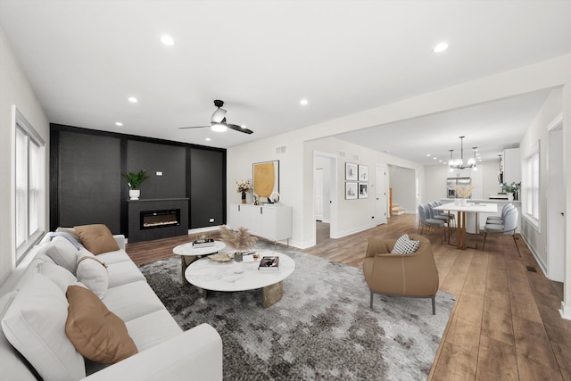 living room with wood-type flooring, a healthy amount of sunlight, ceiling fan with notable chandelier, and a fireplace