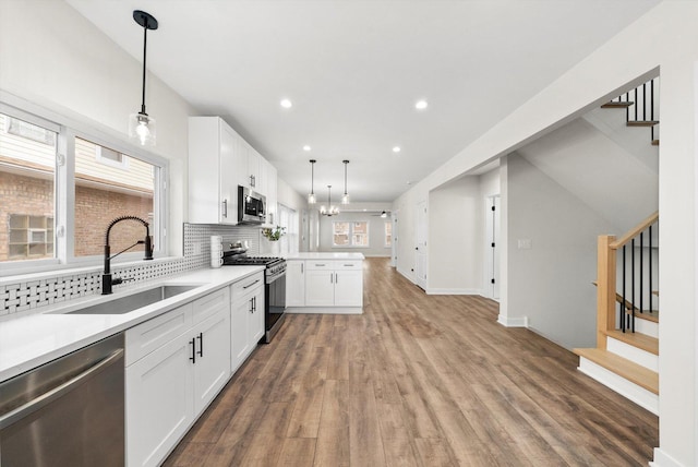 kitchen with sink, white cabinetry, appliances with stainless steel finishes, kitchen peninsula, and pendant lighting