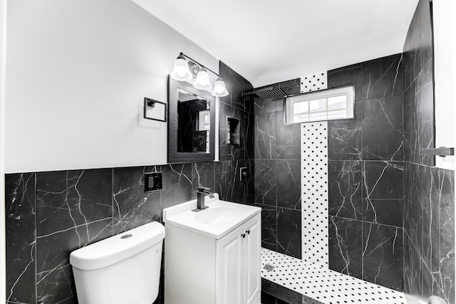 bathroom with vanity, a tile shower, tile walls, and toilet