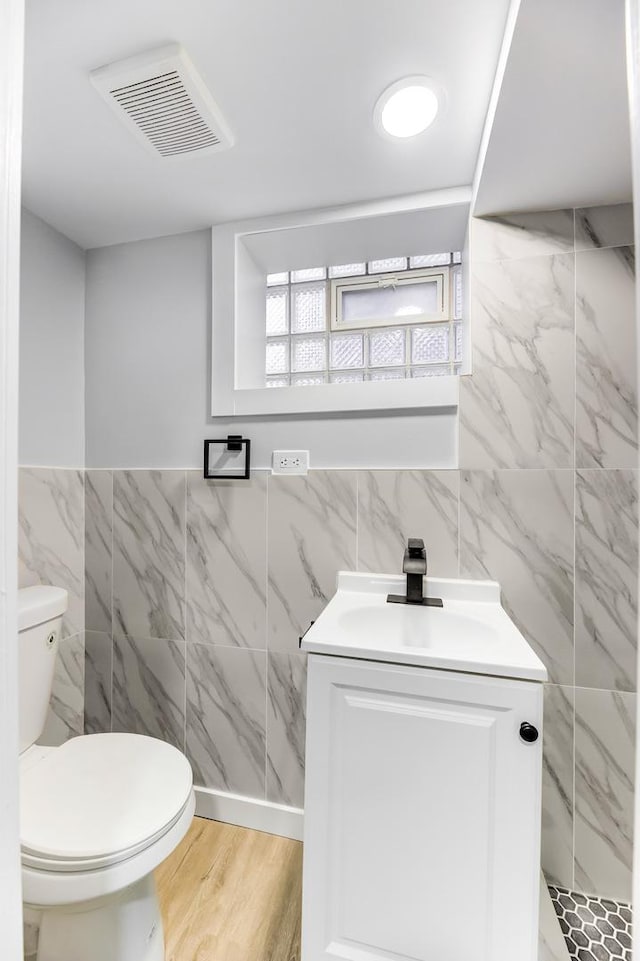 bathroom with wood-type flooring, tile walls, vanity, and toilet